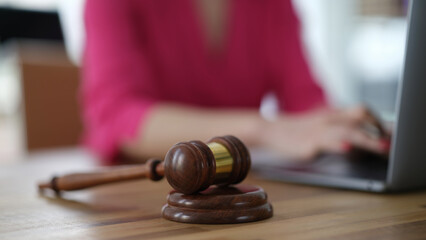 Gavel of judge lying against background of woman behind laptop closeup. Criminal liability for internet fraud concept