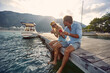 © luckybusiness - Man and woman sitting on the lake pier dangling legs and eat watermelon