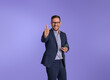 Cheerful male entrepreneur gesturing thumbs up after reading good news over smart phone. Happy young businessman showing perfect and approval sign while standing isolated on blue background