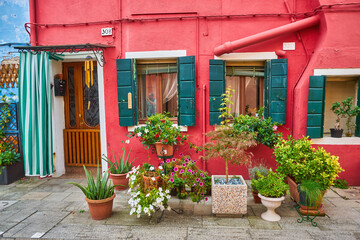 Canvas Print - Door and window with flower on the red facade of the house. Colorful architecture in Burano island, Venice.