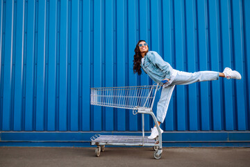 Wall Mural - Young woman with shopping cart having fun near color wall. smilling african woman going shopping. 