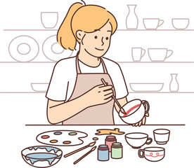 Woman artist draws picture on pottery, wanting to give unique look to handmade products