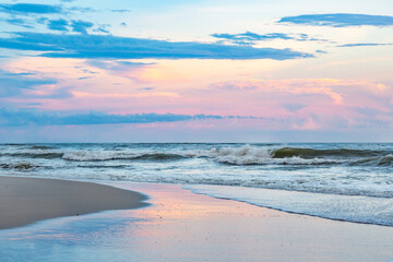 Horizontal blue and pink ocean beach sunset with waves and sky reflections on the wet sand