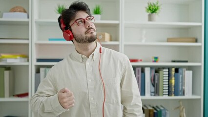 Wall Mural - Young hispanic man student listening to music dancing at library university