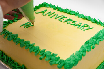 Woman writing with pastry bag on green and yellow birthday cake isolated on white background