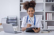 © David - Happy doctor Portrait of young African American woman nurse or doctor smilingusing a laptop writing content at consultation