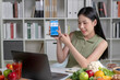 Asian woman professional nutritionist consulting with her client on laptop, surrounded by a variety of fruits, nuts, vegetables, and dietary supplements on the table