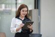 © Songsak C - Smiling young Asian businesswoman holding a digital tablet standing in an office.