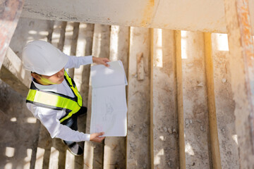 Asian male engineer looks like an architect Looking down at the blueprint On construction site about architectural design in the structural industry Wear a vest and have a helmet.