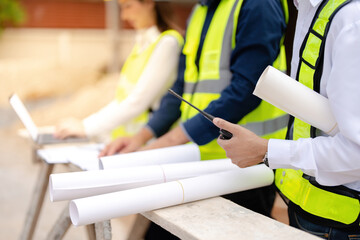 Wall Mural - Close-up shot of hand engineer holding blueprints for architectural project design of large business structure. Contains walkie talkie and tablet.