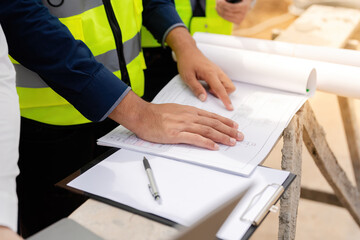 Wall Mural - Close-up of hands of Asian male engineer He's pointing at a blueprint, a listnote, and a pen on his desk. Standing at a large architectural and industrial construction site