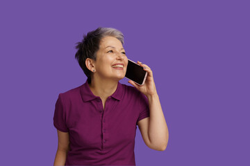 Senior woman with happiness engages in lively conversation on phone. Isolated on violet background, her smile radiates warmth and positivity, capturing essence of joyful communication in digital age