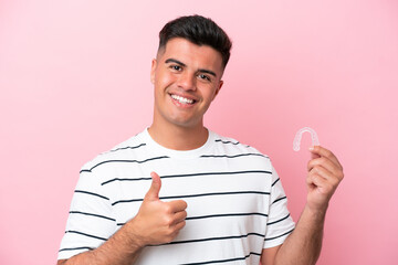 Wall Mural - Young caucasian man holding invisaling isolated on pink background with thumbs up because something good has happened