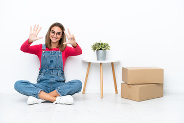 Young caucasian woman sitting on the floor among boxes counting eight with fingers