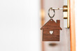 © Nando Vidal - Wooden key chain in the shape of a house with a heart-shaped hole in the center hanging from a key inserted in the lock of a front door of a house.