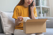 Angry bad, complaint asian young woman opening carton box, received online shopping parcel wrong product order from retail store, using mobile phone talking with support shop want to return package.