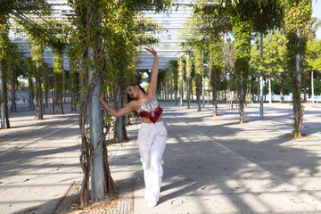 Wall Mural - Latin woman, young and beautiful dancing modern dance in the street in a park and makes different expressions and postures. Concept dance, hip hop, dance, art, action, beauty, youth art.