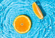 Fresh round orange slices floating in a pool with a rippled saturated blue water. Minimal tropical fruit creative art. Summer refreshment concept.