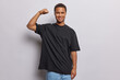© Wayhome Studio - Pleased ethnic man raises arm and shows biceps demonstrates his strength dressed in casual black t shirt and jeans has strong muscles after regular training in gym isolated over white background