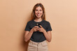 © WHstudio Leushin N - Studio shot of pretty young woman stays connected through social networks holds mobile phone in hands has happy smile on face wears casual black t shirt and trousers isolated over brown background