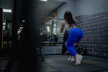 A Sports Girl In Blue Leggings And A Sexy Body Warms Up In Front Of A Mirror At A Workout In A Gym With Exercise Equipment	