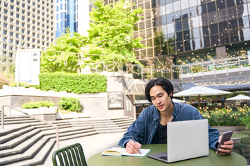 Wall Mural - Asian writer man using laptop computer taking notes, working project outdoors