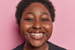 © WHstudio Leushin N - Headshot of radiant curly African girl beams with contagious smile shows white teeth has eyes full of pure joy spreads positivity and warmth to all who behold it poses against pink background.