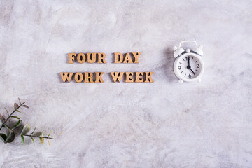 Four day work week concept with wooden letters and alarm clock on gray background
