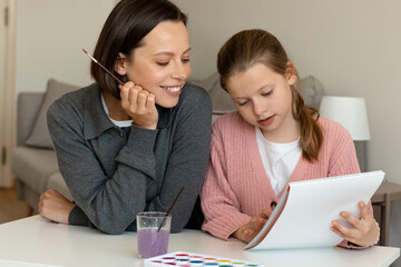 Wall Mural - Happy caucasian middle aged mother and little daughter enjoy free time, painting with paints in living room