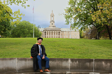 A Doctoral graduate  sitting and looking at camera with main campus building behind