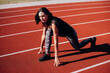© VlaDee - Full body side view of focused young female sprinter in low start position ready to run from starting on red track of stadium