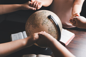 Wall Mural - Christian group praying for globe and people around the world on wooden table with bible. Christian small group holding hands and praying together around a wooden table with bible page in homeroom.