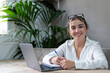 © Daniel - Portrait of smiling millennial caucasian female student sit at desk at home study online on laptop. Happy young cheerful woman use computer take distant course or training. Education concept..