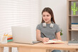 © New Africa - Cute girl with headphones writing in notepad near laptop at desk in room. Home workplace