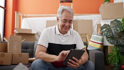 Poster - Middle age man with grey hair sitting on the sofa using tablet at new home