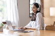 © David - Young adult happy smiling Hispanic Asian student wearing headphones talking on online chat meeting using laptop in home office. College female student learning business education remotely.