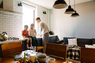 Wall Mural - Father washing dishes while his kids watching cartoons on tablet in kitchen