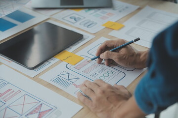 Close up ux developer and ui designer brainstorming about mobile app interface wireframe design on table with customer breif and color code at modern office.Creative digital development agency