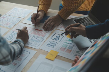 Close up ux developer and ui designer brainstorming about mobile app interface wireframe design on table with customer breif and color code at modern office.Creative digital development agency