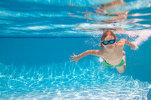 Child In Swimming In Pool. Funny Little Boy Swims Underwater In The Pool. Underwater Kids Portrait From Under The Water. Summer Holiday. Kids Weekend.