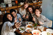 © Drobot Dean - Group of cheerful friends taking selfie and drinking wine while dining in restaurant