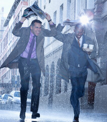 Wall Mural - Businessmen carrying coffee and covering heads with newspaper in rain