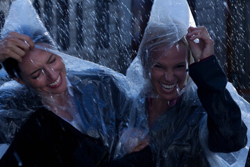 Laughing businesswomen wearing ponchos in rain