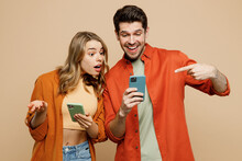 Young Happy Confused Couple Two Friends Family Man Woman Wear Casual Clothes Hold Use Point Finger On Mobile Cell Phone Together Isolated On Pastel Plain Light Beige Color Background Studio Portrait.