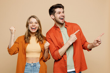 Wall Mural - Young couple two friends family man woman wear casual clothes point index finger aside on area mock up do winner gesture together isolated on pastel plain light beige color background studio portrait.