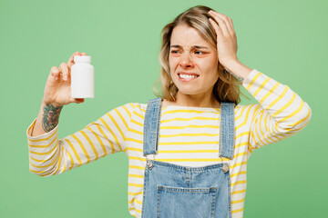 Wall Mural - Sick unhealthy ill allergic woman has red watery eyes runny stuffy sore nose suffer from allergy trigger symptoms hay fever hold container bottle with drugs isolated on plain green background studio .