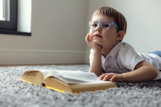 Wall Mural - smart little child reads a book, a boy with glasses lies at home, an open book in front of him