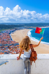 Wall Mural - woman tourist holding portuguese flag enjoying beautiful view of panoramic beach view- nazare