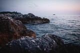 Fototapeta Morze - Sea waves splash over the rocky shore at sunset with a pink sky in the background