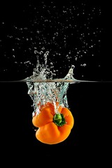 Sticker - Closeup shot of an orange bell pepper dropping into the water with splashes on a black background